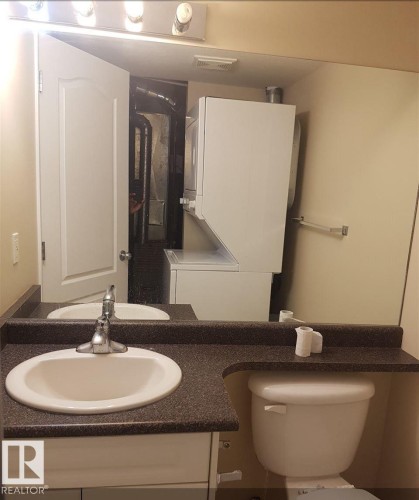 Vanity with integrated sink, solid surface countertop, wall-mounted light fixture, toilet, and a stacked washer and dryer unit - #9 2505 42 St Nw, Edmonton, AB 