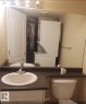 Vanity with integrated sink, solid surface countertop, wall-mounted light fixture, toilet, and a stacked washer and dryer unit - #9 2505 42 St Nw, Edmonton, AB 