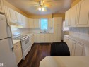Kitchen featuring extensive white cabinetry, wood-finish flooring, a ceiling fan with integrated lighting, and a white tile backsplash - 10438 147 Street Nw, Edmonton, AB 