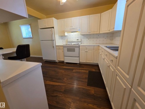 Kitchen featuring wood-finish flooring, white cabinetry, white appliances, and a white countertop - 10438 147 Street Nw, Edmonton, AB 
