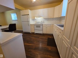 Kitchen featuring wood-finish flooring, white cabinetry, white appliances, and a white countertop - 