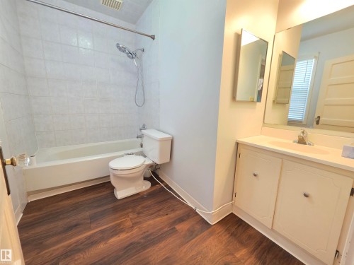 Bathroom featuring wood-finish flooring, a white vanity with integrated sink, a built-in medicine cabinet, and a bathtub with tile surround - 10438 147 Street Nw, Edmonton, AB 