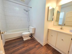 Bathroom featuring wood-finish flooring, a white vanity with integrated sink, a built-in medicine cabinet, and a bathtub with tile surround - 