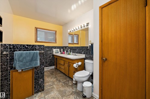 Bathroom featuring a wood-finish vanity with an integrated sink, a wall-mounted mirror, and tile flooring - 10621 60A Avenue Nw, Edmonton, AB 
