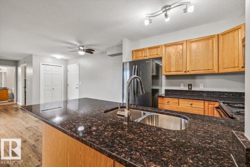 Kitchen featuring a double basin sink with a high-arc faucet, wood-finish cabinetry, and black appliances - #110 4309 33 St, Stony Plain, AB 