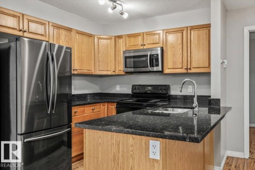 Wood-finish cabinetry paired with dark countertops, stainless steel appliances, and a built-in kitchen sink with a gooseneck faucet - #110 4309 33 St, Stony Plain, AB 