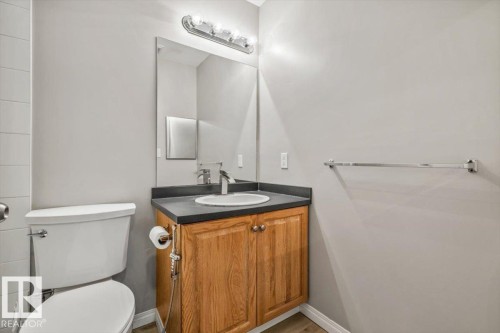 Wood-finish flooring, wood cabinetry with dual doors, white toilet, and a vanity with an integrated sink - #110 4309 33 St, Stony Plain, AB 