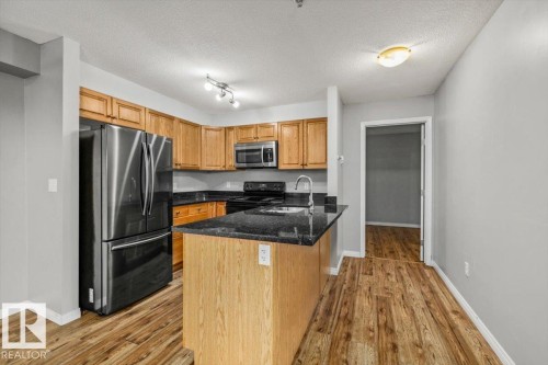 Kitchen featuring wood-finish flooring, wood cabinetry, dark countertops, and stainless steel appliances - #110 4309 33 St, Stony Plain, AB 