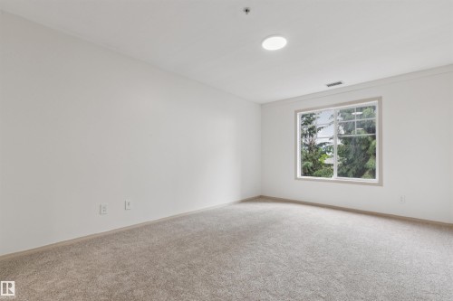 Bright room featuring a large window, plush carpeting, white walls, and a circular ceiling light fixture - #353 2096 Blackmud Creek Dr Sw, Edmonton, AB - Indoor Photo Showing Other Room