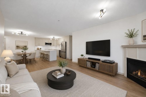 Living area featuring wood-finish flooring, a corner fireplace with a traditional mantel, and recessed ceiling lighting (virtually staged) - #353 2096 Blackmud Creek Dr Sw, Edmonton, AB - Indoor Photo Showing Living Room With Fireplace