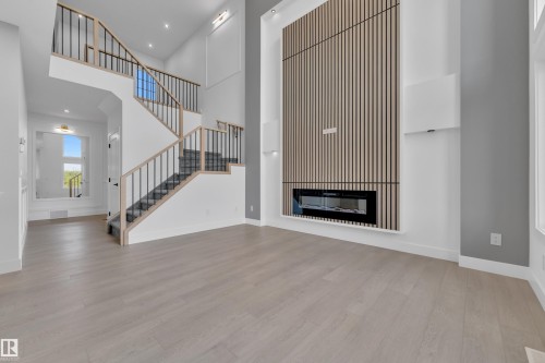Two-story ceiling, wood-finish flooring, staircase with wood and metal railing, integrated electric fireplace, and a feature wall with vertical wood slat accents - 1129 Starling Drive Nw, Edmonton, AB 