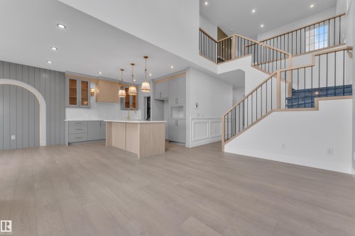 Light wood-finish flooring, two-tone cabinetry, kitchen island with pendant lighting, wainscoting, and a multi-level staircase with iron balusters - 1129 Starling Drive Nw, Edmonton, AB 