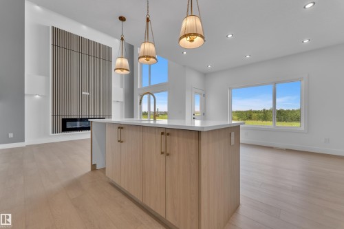 Open-concept interior featuring light wood-finish flooring, a modern kitchen island with a white countertop, and a built-in fireplace with vertical paneling - 1129 Starling Drive Nw, Edmonton, AB 
