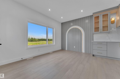 Light wood-finish flooring, recessed ceiling lighting, a large window, a decorative arched niche, and built-in cabinetry with glass-front uppers - 1129 Starling Drive Nw, Edmonton, AB 