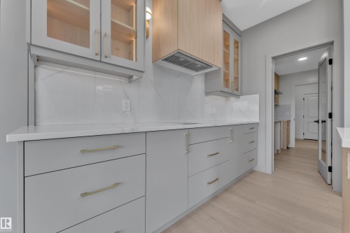Custom cabinetry with glass door accents, under-cabinet lighting, light-toned wood-finish flooring, white countertop, and a tiled backsplash - 1129 Starling Drive Nw, Edmonton, AB 