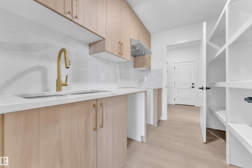 Light wood-finish cabinetry with gold-tone hardware, white countertops, a gold-tone gooseneck faucet, and a stainless steel range hood - 1129 Starling Drive Nw, Edmonton, AB 