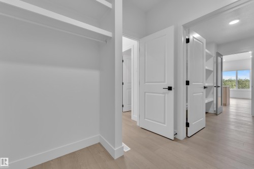 Built-in closet shelving and hanging rod, modern interior doors with matte black hardware, light wood-finish flooring, recessed lighting, and built-in hallway shelving - 1129 Starling Drive Nw, Edmonton, AB 
