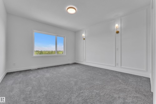 Spacious room with gray carpet, a wide window, decorative wall molding, two wall sconces, and a flush-mount ceiling light fixture - 1129 Starling Drive Nw, Edmonton, AB 