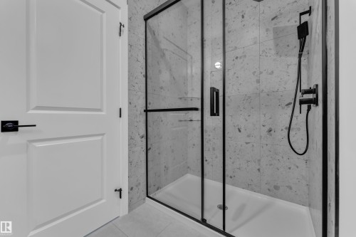 Glass-enclosed shower with matte black fixtures, integrated shelving, and a patterned tile surround - 1129 Starling Drive Nw, Edmonton, AB 