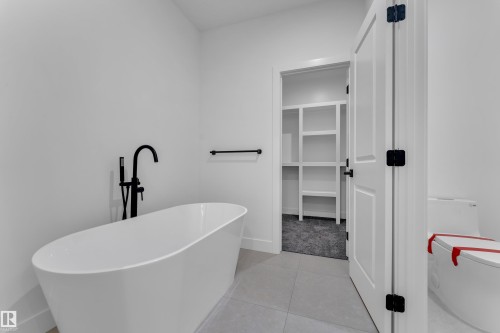 Freestanding soaking tub with a matte black floor-mounted faucet, complemented by light-toned tile flooring - 1129 Starling Drive Nw, Edmonton, AB 