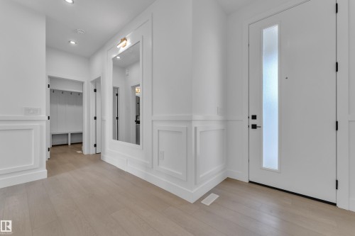 Wide plank wood-finish flooring, white paneling, recessed lighting, built-in mudroom bench with coat hooks, and a front door with a vertical frosted glass insert - 1129 Starling Drive Nw, Edmonton, AB 