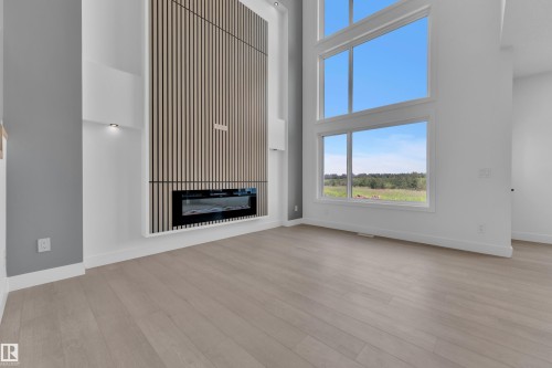 Modern living space featuring soaring ceilings, expansive windows framing scenic vistas, wide-plank wood-finish flooring, and a striking linear fireplace with vertical slat surround detail - 1129 Starling Drive Nw, Edmonton, AB 