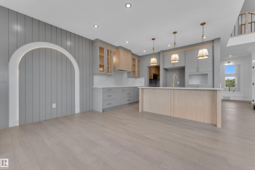 Recessed lighting, wood-finish flooring, an arched wall feature, a kitchen island with pendant lighting, and a gold-finish kitchen faucet - 1129 Starling Drive Nw, Edmonton, AB 