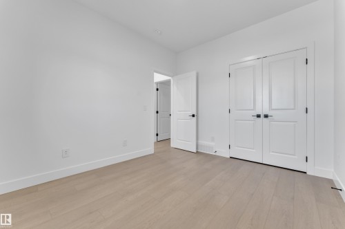 Light wood-finish flooring, white walls, and white paneled doors with matte black hardware - 1129 Starling Drive Nw, Edmonton, AB 