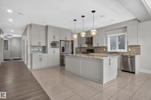 Kitchen featuring light gray cabinetry, stainless steel appliances, a center island with a light-toned countertop, and mosaic tile backsplash - 2219 22 Street Nw, Edmonton, AB 