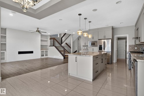 Open-concept living area featuring a kitchen island with pendant lighting, stainless steel appliances, a built-in electric fireplace, and integrated shelving - 2219 22 Street Nw, Edmonton, AB 