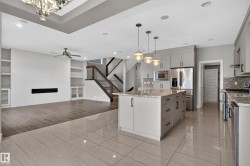 Open-concept living area featuring a kitchen island with pendant lighting, stainless steel appliances, a built-in electric fireplace, and integrated shelving - 