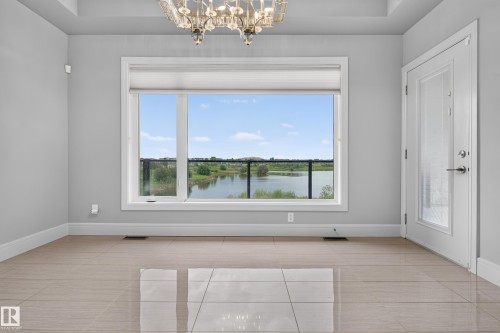 Recessed ceiling with an ornate chandelier, large window with roller shades, white trim, light-toned tile flooring, and a glass-paneled door - 2219 22 Street Nw, Edmonton, AB 