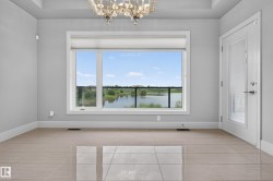 Recessed ceiling with an ornate chandelier, large window with roller shades, white trim, light-toned tile flooring, and a glass-paneled door - 