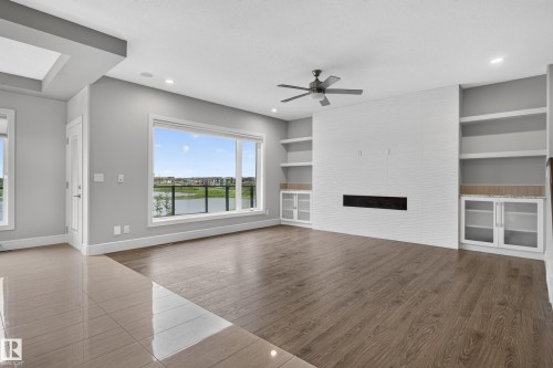 Expansive living area with wood-finish flooring, a linear fireplace set into a white brick-patterned wall, and built-in shelving with cabinetry - 2219 22 Street Nw, Edmonton, AB 