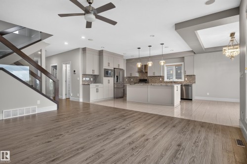 Open-concept living area with wood-finish flooring, a kitchen featuring light gray cabinetry, stainless steel appliances, and a tiled backsplash - 2219 22 Street Nw, Edmonton, AB 