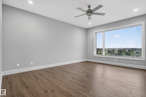 Spacious room with wood-finish flooring, a large picture window, recessed lighting, a ceiling fan, and white baseboards - 2219 22 Street Nw, Edmonton, AB 