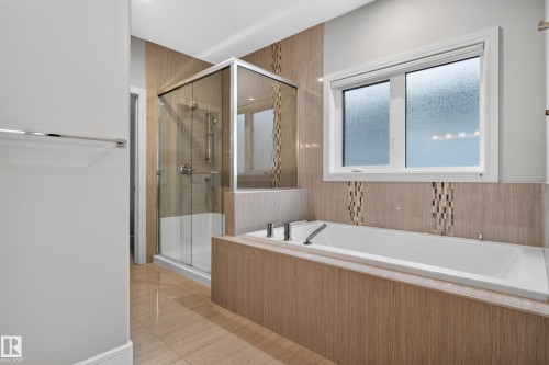 Tiled flooring with a white soaking tub, integrated fixtures, a frosted window, and a glass-enclosed shower - 2219 22 Street Nw, Edmonton, AB 