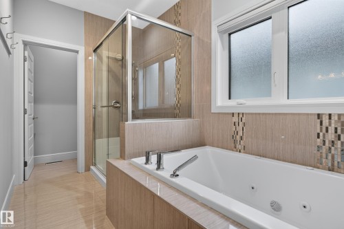 White soaking tub with deck-mounted chrome fixtures, glass-enclosed shower, and tiled walls with decorative mosaic accents - 2219 22 Street Nw, Edmonton, AB 