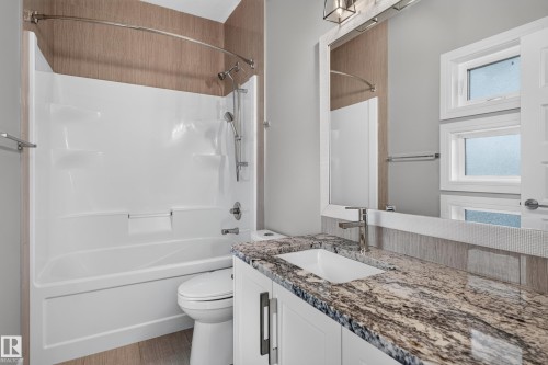 White shower/tub combination with a curved shower rod, vanity with a stone countertop, undermount sink, and brushed nickel faucet, framed mirror, and natural light from multiple windows - 2219 22 Street Nw, Edmonton, AB 
