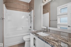 White shower/tub combination with a curved shower rod, vanity with a stone countertop, undermount sink, and brushed nickel faucet, framed mirror, and natural light from multiple windows - 