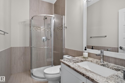 Full bathroom featuring a curved glass shower enclosure, a vanity with a stone countertop, an integrated rectangular sink, a chrome faucet, and a wall-mounted mirror - 2219 22 Street Nw, Edmonton, AB 