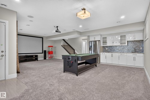 Recessed lighting throughout, built-in projection screen, wet bar featuring white cabinetry and a mosaic tile backsplash, and wood-finish stairs with a dark railing - 2219 22 Street Nw, Edmonton, AB 
