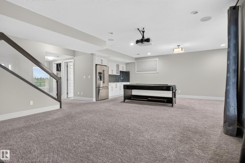 Expansive carpeted area featuring a wet bar with white cabinetry, stainless steel refrigerator, and dark countertops - 2219 22 Street Nw, Edmonton, AB 