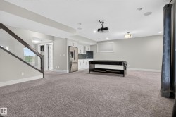 Expansive carpeted area featuring a wet bar with white cabinetry, stainless steel refrigerator, and dark countertops - 
