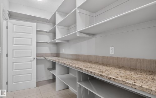 Spacious pantry featuring extensive open shelving, wrap-around counter space with a stone-finish surface, and light-toned tile flooring - 2219 22 Street Nw, Edmonton, AB 
