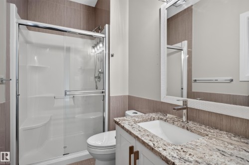 Shower with sliding glass enclosure, vanity with stone countertop, undermount sink, and wall-mounted mirror - 2219 22 Street Nw, Edmonton, AB 