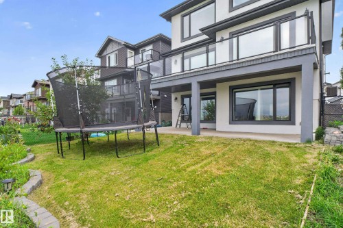 Rear exterior featuring a ground-level patio, upper-level balcony with glass railing, and a sloped lawn - 2219 22 Street Nw, Edmonton, AB 