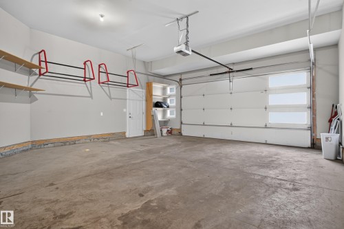 Spacious garage with concrete flooring, overhead garage door with integrated windows, built-in shelving, and a pedestrian access door - 2219 22 Street Nw, Edmonton, AB 