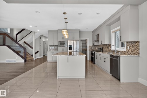 Contemporary kitchen featuring a center island, pendant lighting, light gray cabinetry, stainless steel appliances, and a mosaic tile backsplash - 2219 22 Street Nw, Edmonton, AB 