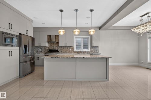 Kitchen featuring light grey cabinetry, stainless steel appliances, a center island with pendant lighting, and a mosaic tile backsplash - 2219 22 Street Nw, Edmonton, AB 